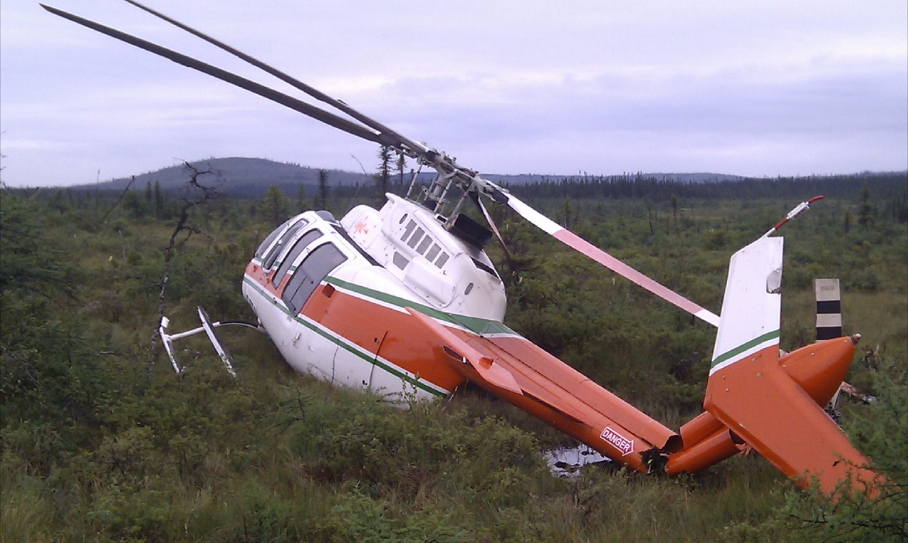 A photograph shows the helicopter, tilted slightly rightward and damaged, at the grassy site of the occurrence.